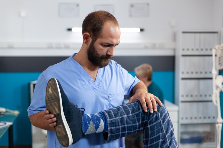 Chiropractor stretching leg of elder patient for physiotherapy